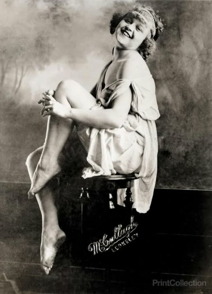 Vintage photo of a smiling woman in a draped dress, sitting gracefully on a pedestal, resonating history.