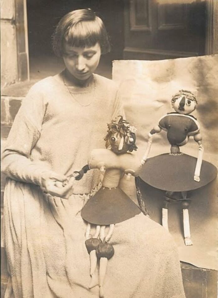 Woman from a hundred years ago holding vintage dolls, showcasing timeless creativity and craftsmanship.
