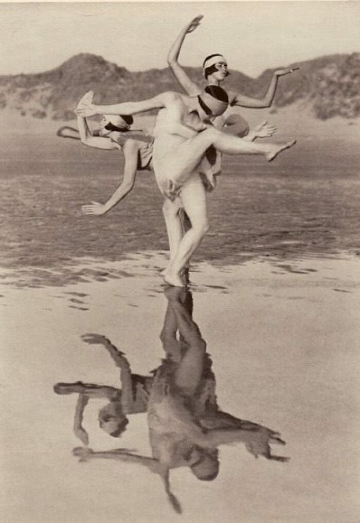 Dancers performing on a beach, their reflections evident in the water, showcasing timeless elegance from over a century ago.