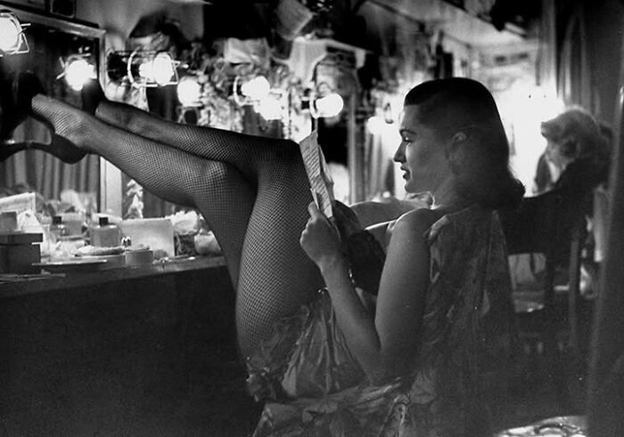 Vintage photo of a woman in fishnet tights relaxing backstage with a magazine, highlighting timeless moments from the past.
