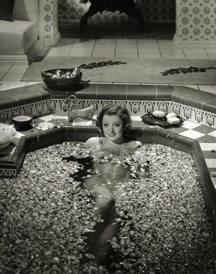 Vintage photo of a woman in an ornate bath surrounded by petals, embodying timeless elegance.