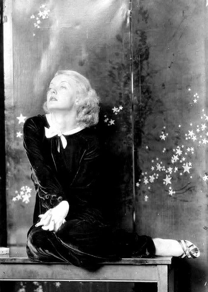 Woman in vintage attire sitting on a table, surrounded by star motifs, evoking timeless elegance from over a hundred years ago.