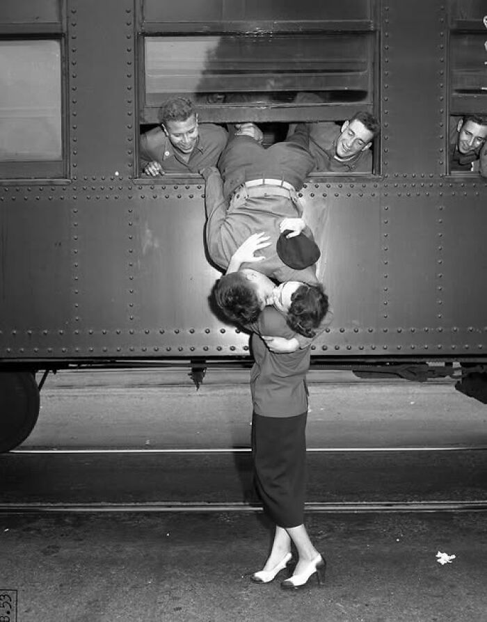 A soldier kisses a woman goodbye through a train window, capturing a moment that resonates today.