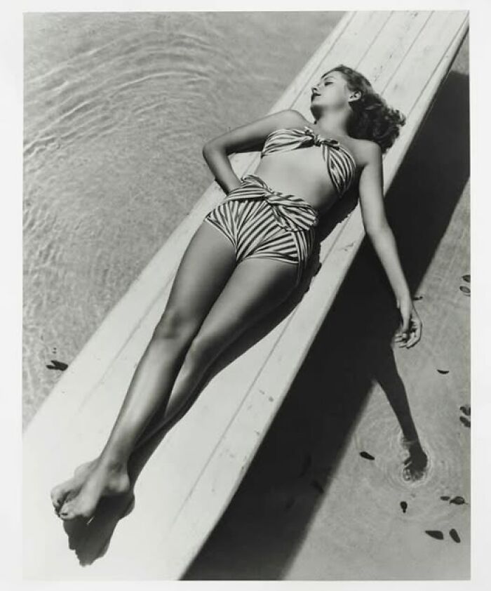 Woman in vintage swimsuit lounging on a diving board beside a pool, reflecting timeless fashion over the years.
