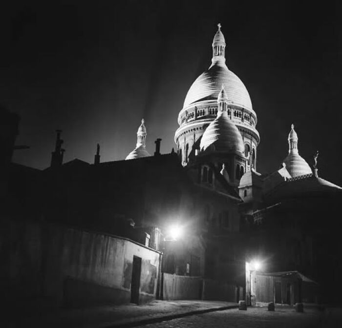 Historic black and white photo of Sacré-Cœur Basilica at night, showcasing timeless architecture with domes and street lights.