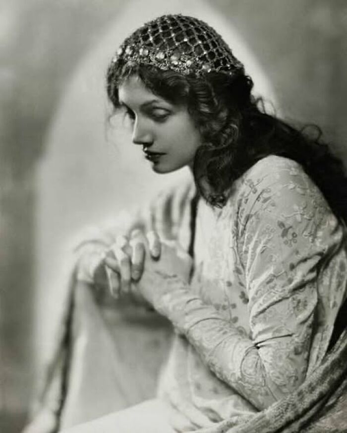 A woman from the early 1900s wearing an ornate headpiece and patterned dress, illustrating historical fashion that resonates today.