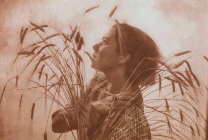 A woman from a bygone era holds wheat stalks, highlighting themes that continue to resonate today.