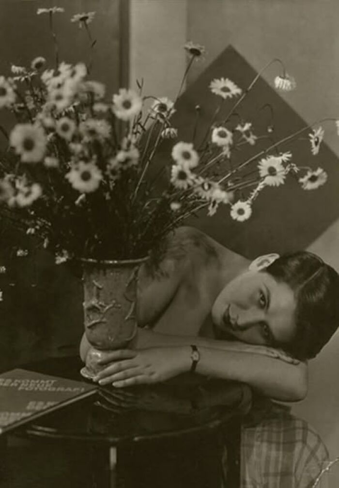 Vintage photo of a woman resting her head on a table with flowers, evoking historical resonance from over a century ago.