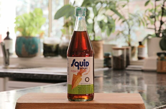 Bottle of fish sauce on a kitchen counter with plants in the background.