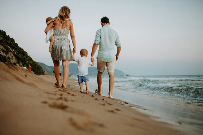 Family walking on a sandy beach near the ocean at sunset, holding hands and enjoying time together.