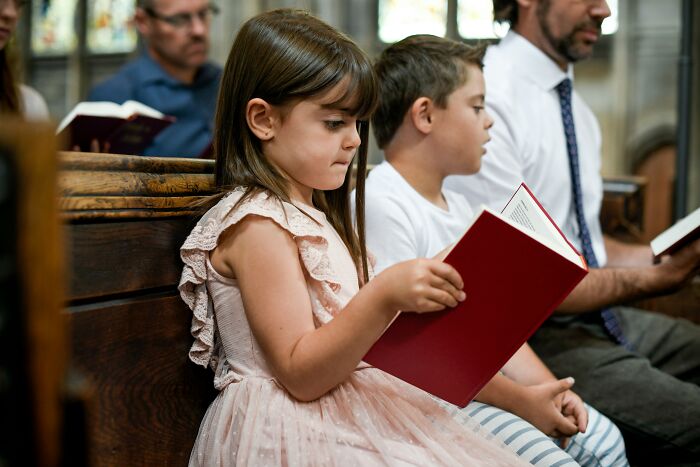 Child reading a book in church, highlighting parenting decisions about religious practices.