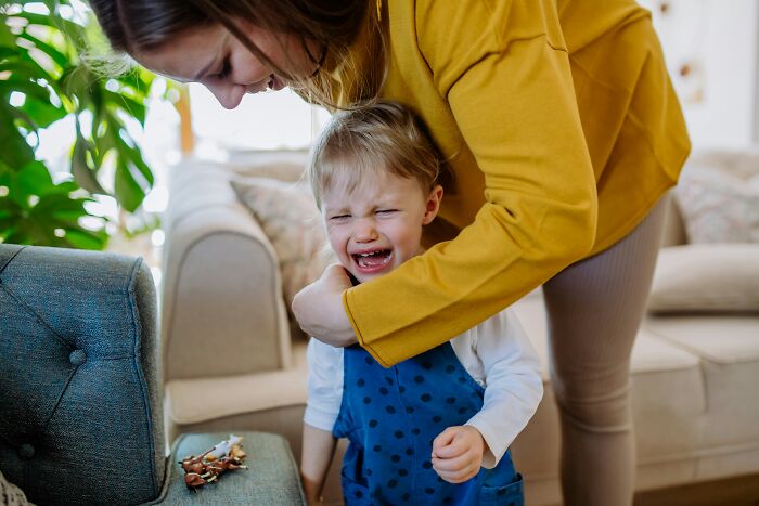 Adult playfully interacting with a laughing toddler in a cozy living room.