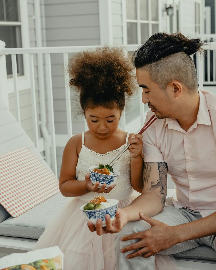 Man and child eating on a porch, highlighting a parenting moment involving shared meals.