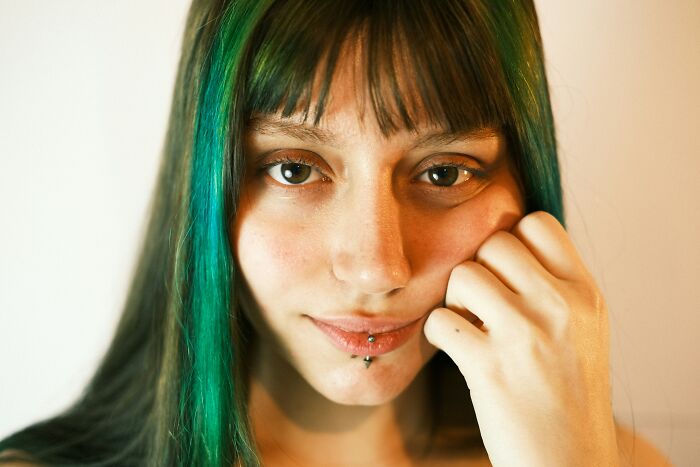 Young woman with green hair and a piercing, contemplating a decision about parenting choices.