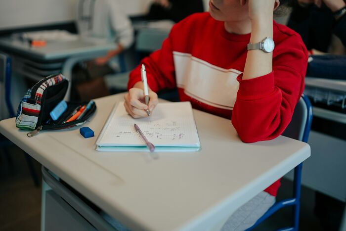 Student in a red sweater taking notes at a desk, focused on studying, highlighting educational habits parents influence.