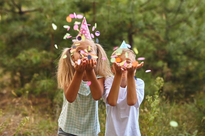Children at a birthday party outdoors, wearing party hats and throwing confetti, in a joyful setting.