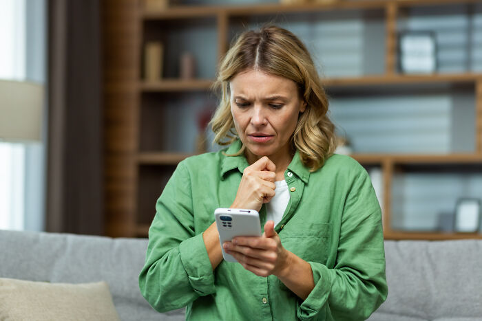 Woman in a green shirt looking concerned at her phone during a birthday party.