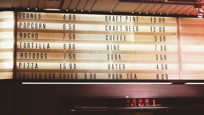 Menu board with fast food items like scones, hotdogs, and drinks like coffee, soda; prices displayed next to each item.
