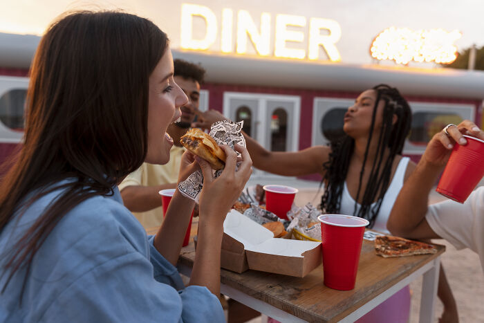 Group of friends enjoying fast food at an outdoor diner with red cups and a burger in hand.