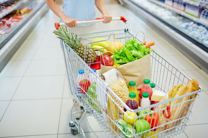 A person pushing a grocery cart filled with fresh produce and healthy groceries, symbolizing a quit from fast food.