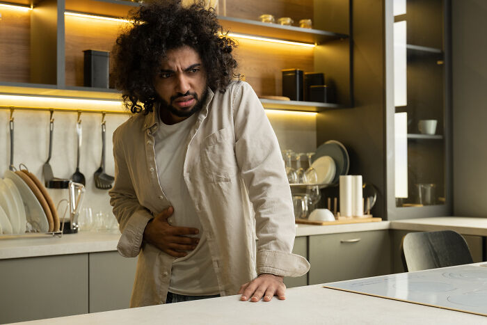 Person in a kitchen holding their stomach, looking uncomfortable, representing reasons to quit fast food.
