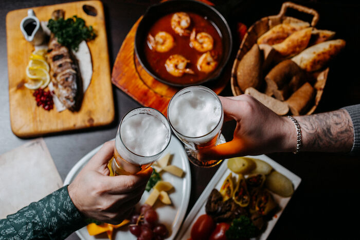 Two people toasting with beer over a table with non-fast food dishes, like shrimp and bread, illustrating reasons to quit fast food.