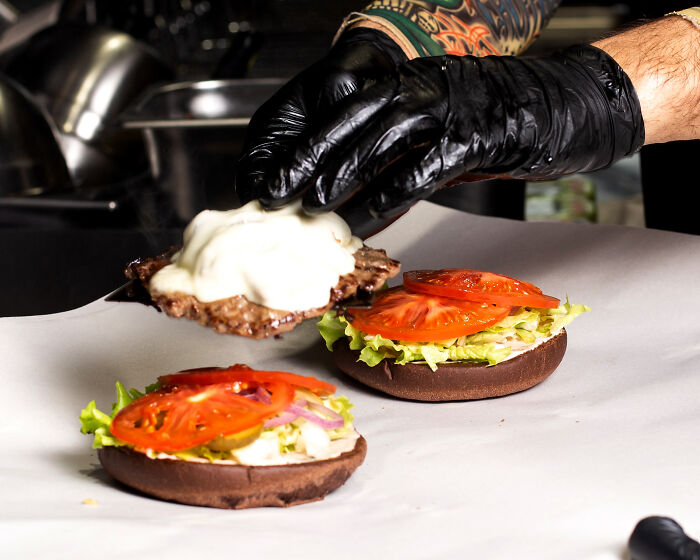 Fast food preparation with black gloved hands assembling a burger, highlighting reasons to quit fast food.