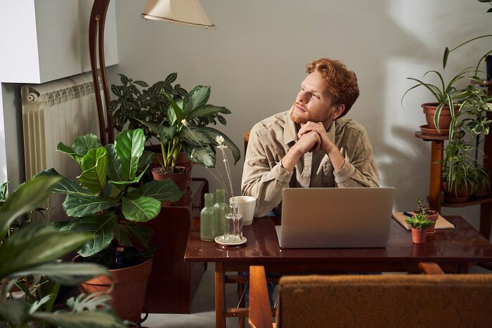 Man reflecting while sitting at a desk with a laptop surrounded by plants, symbolizing decision to quit fast food.