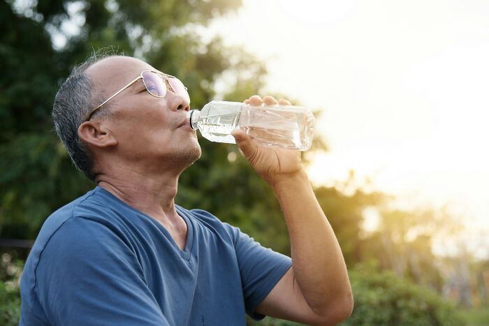 A man in sunglasses and blue shirt enjoying a drink of water outdoors, representing quitting fast food habits.