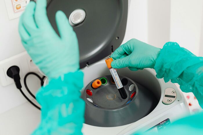 Lab technician wearing gloves placing a vial in a centrifuge, focusing on analysis preparation.