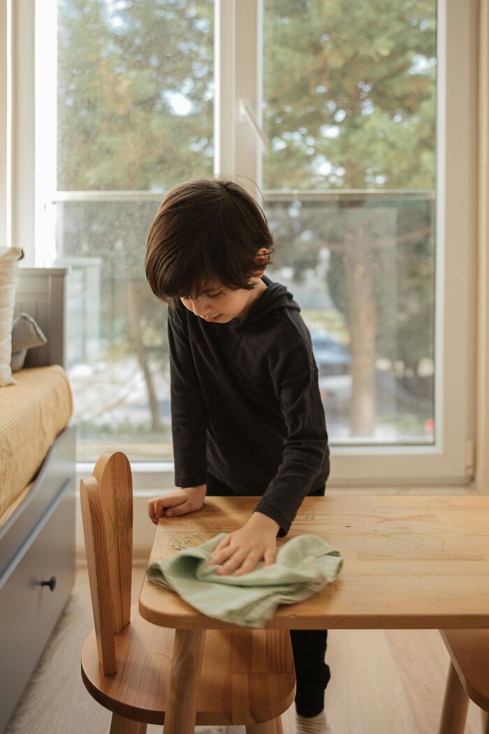 Child cleaning a table with a cloth, demonstrating parenting hacks and reverse psychology techniques.