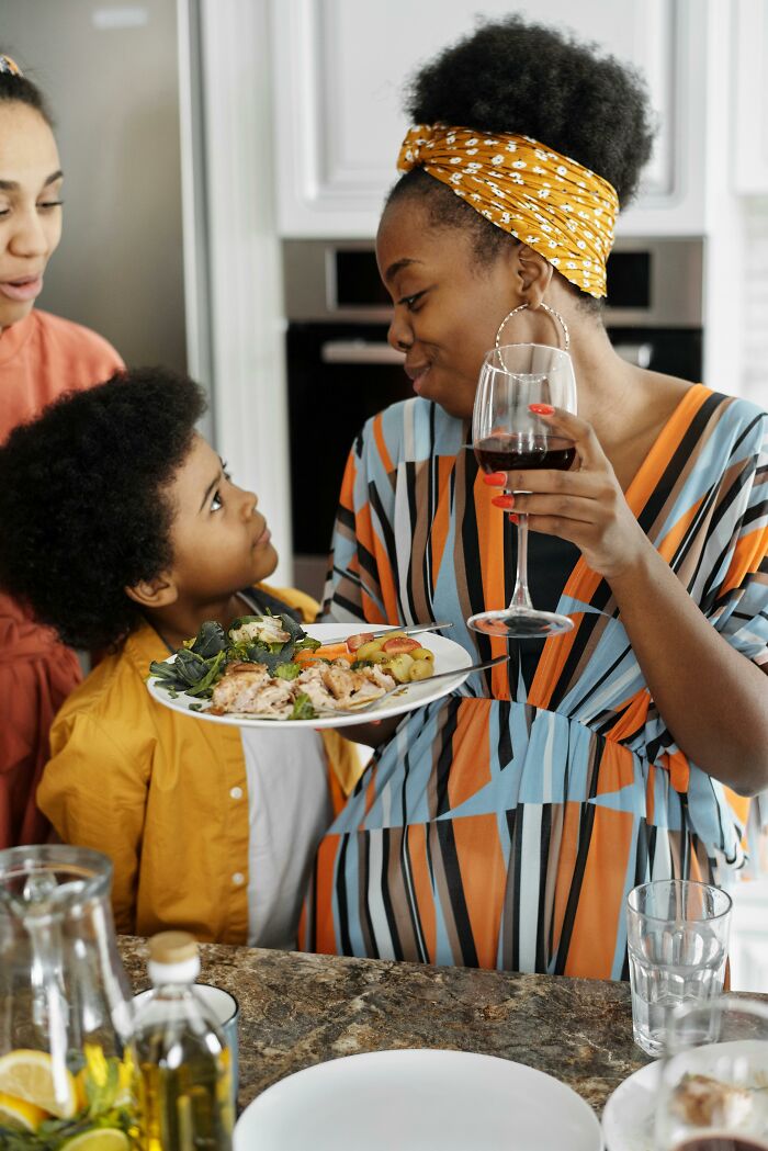 Mother and child in kitchen, employing parenting hacks and reverse psychology during mealtime, with wine and food.