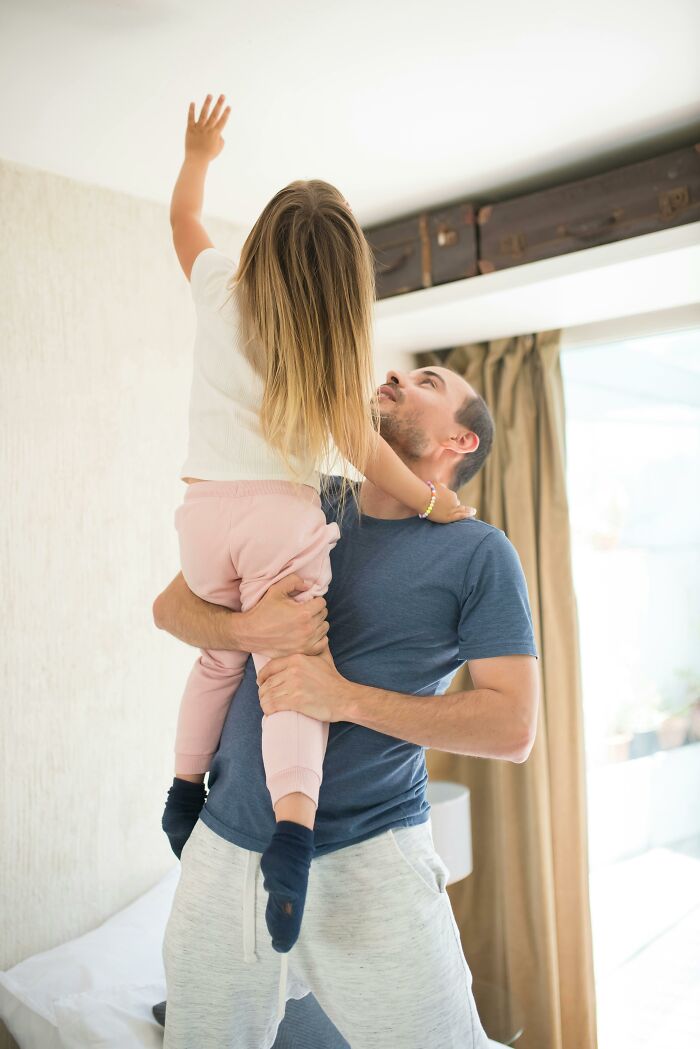 Parent holding child up, using reverse psychology trick at home, child reaching towards ceiling.