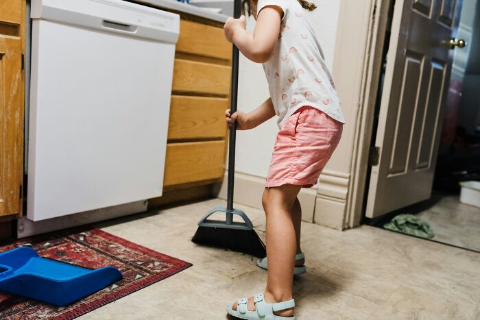 Child using a broom in the kitchen, demonstrating a parent hack for encouraging tidiness at home.