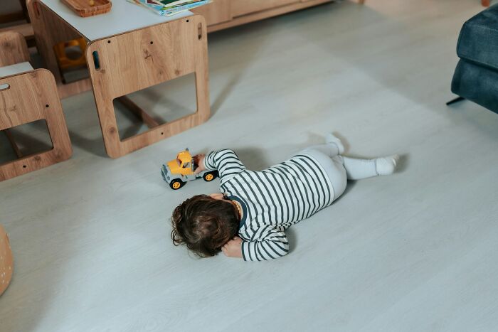 Child lying on floor, playing with toy truck in a home setting, reflecting parenting hacks and reverse psychology.