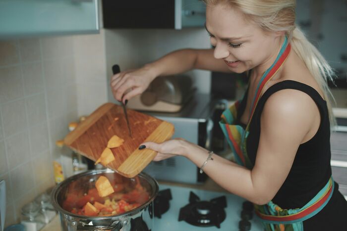 Woman in apron cooking vegetables, illustrating challenges of adulthood in a kitchen setting.