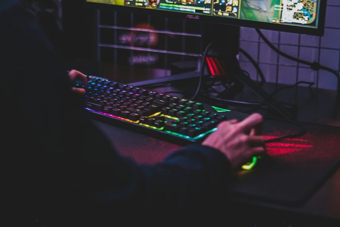 Person using a keyboard with rainbow backlight while gaming, highlighting adulthood challenges and technology.