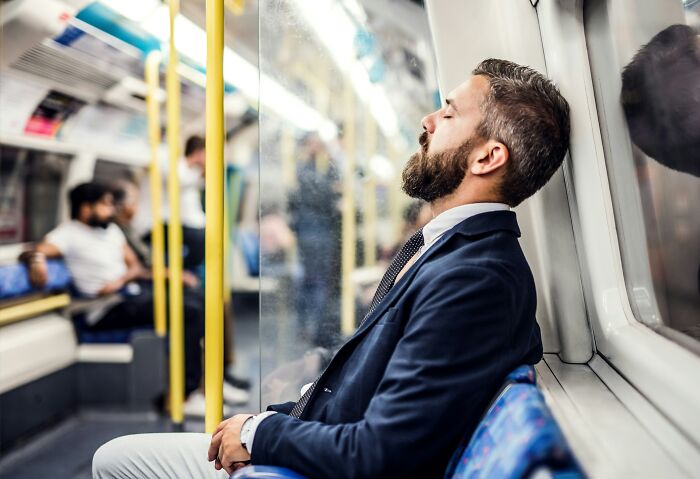 Man in a suit asleep on a subway train, illustrating unexpected challenges of adulthood.