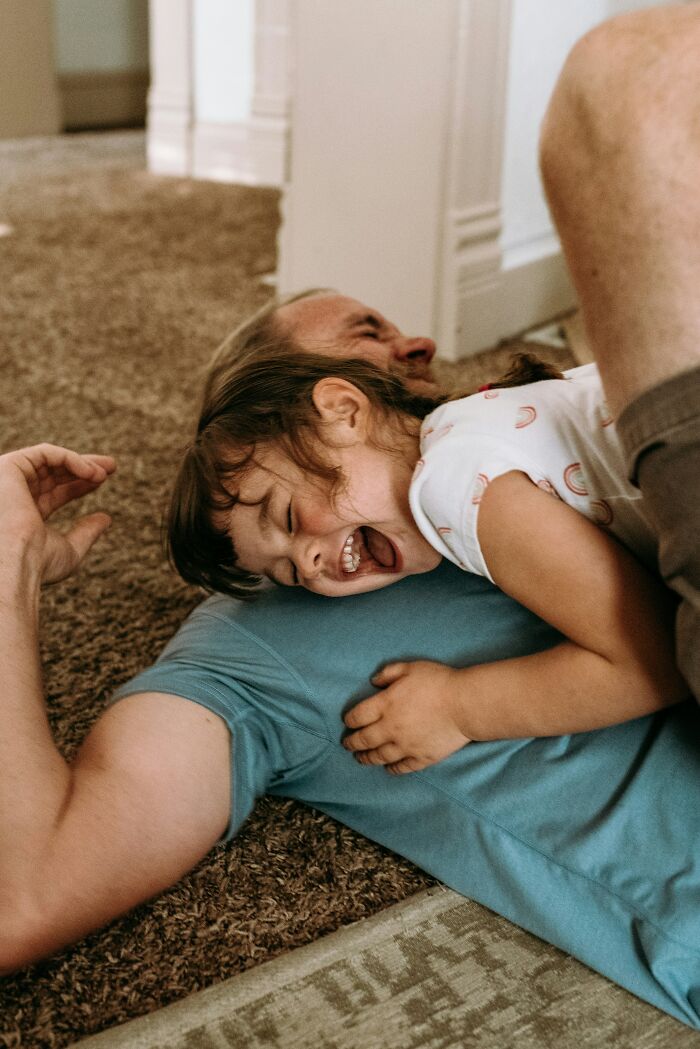 Child laughing while playing with an adult on a carpet, illustrating challenges of adulthood through parenting moments.