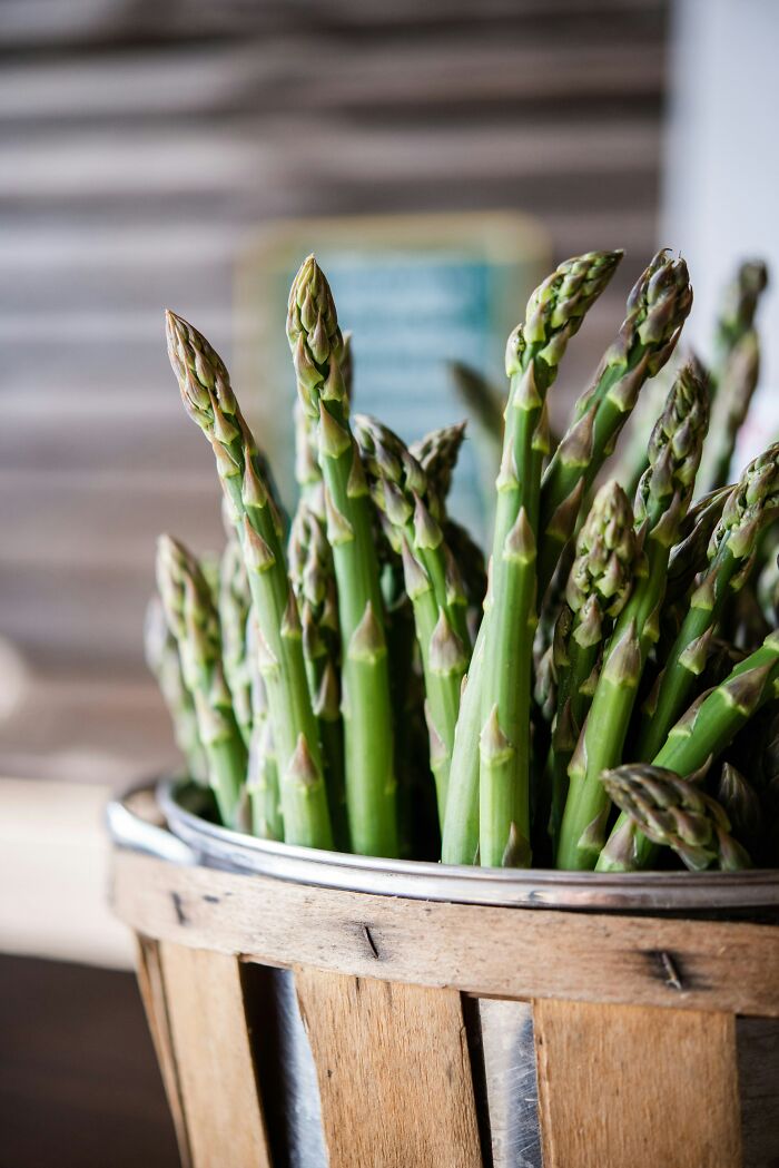 Fresh asparagus spears in a wooden basket, ready for cooking, representing one of the challenges of meal prep in adulthood.