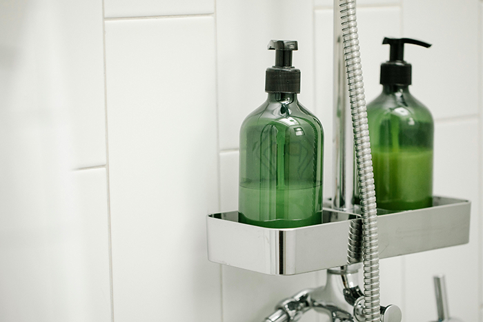 Green shower bottle in a chrome holder, related to not showering regularly.