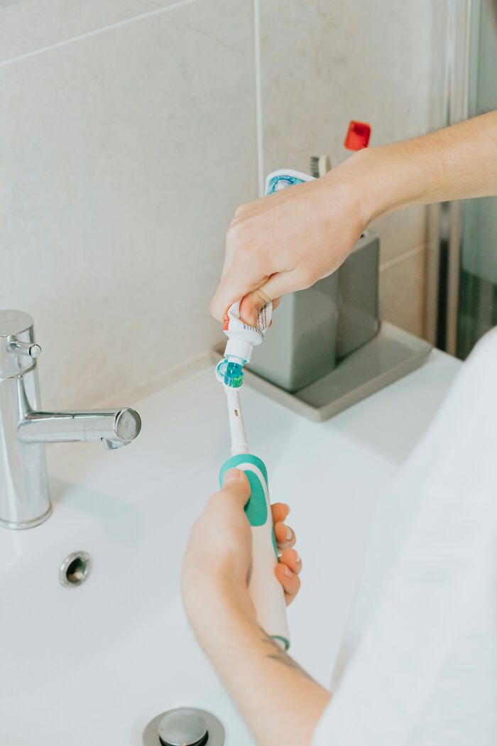 Person applying toothpaste to an electric toothbrush, part of a thread on life improvements.