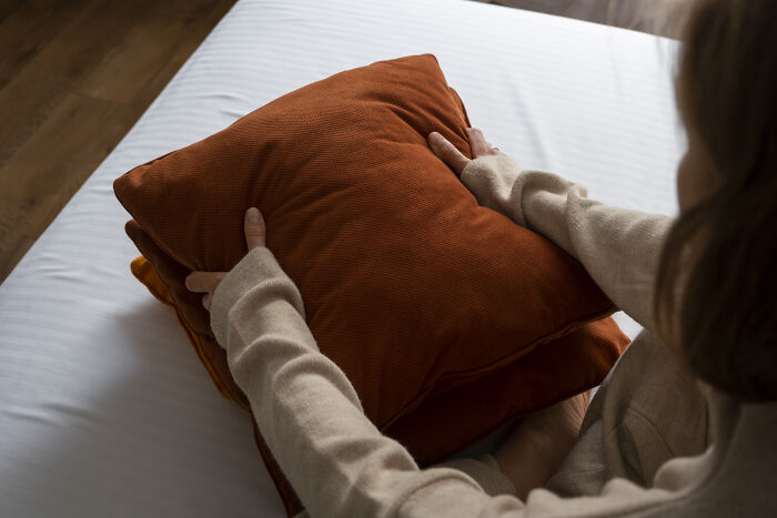 Person holding an orange pillow on a bed, representing simple Valentine's gift ideas.
