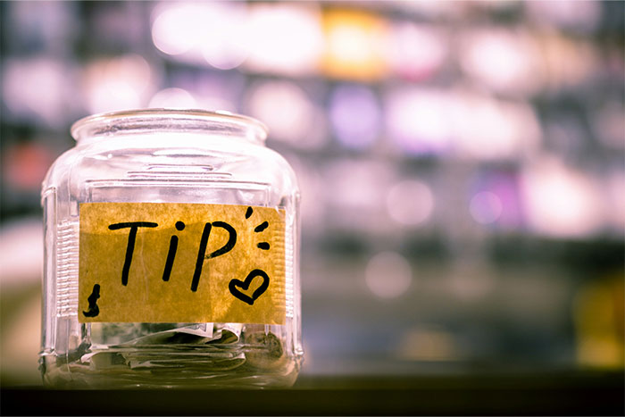 Tip jar filled with coins, representing a pay it forward theme in a blurred background.
