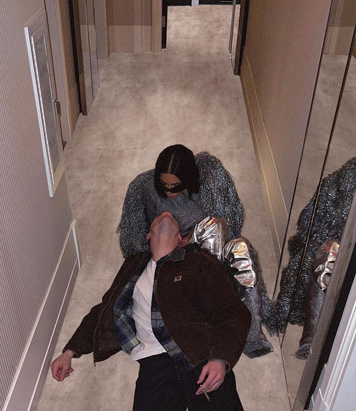 Kim Kardashian in shiny outfit kneels over Pete Davidson lying on hallway floor; reflecting love story rumors.