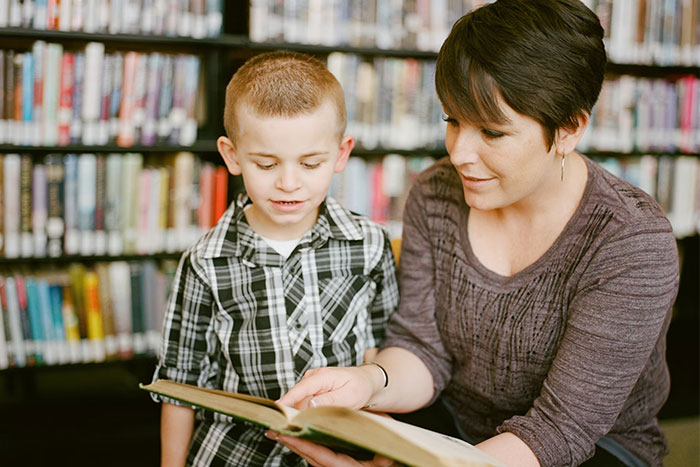 A woman and child in a library, reading a book together, sharing a moment amidst shelves of books.