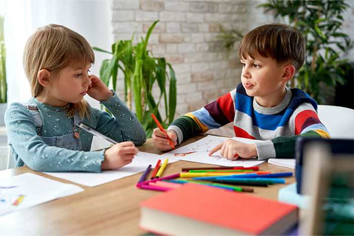 Two children holding colored pencils at a table, illustrating petty grudges creatively with drawings.