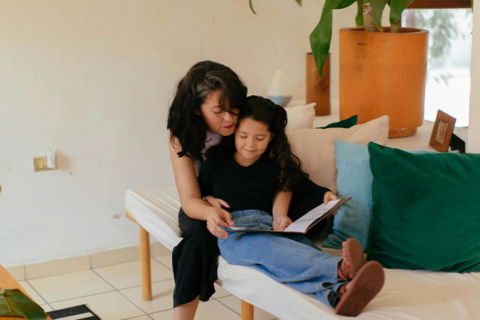 A woman and child sitting on a couch reading together, surrounded by green cushions, depicting shared moments.