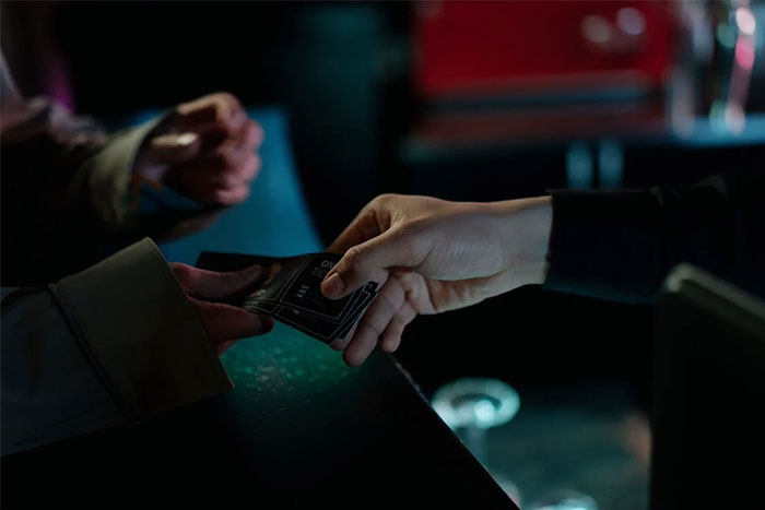 Two people exchanging credit cards in a dimly lit setting, symbolizing petty grudges.