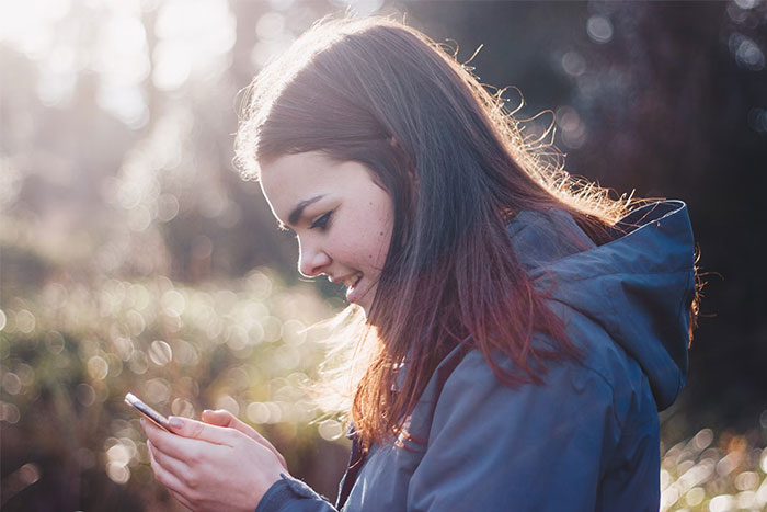 Woman outdoors in a jacket, smiling at her phone, representing the concept of holding petty grudges.